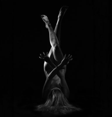Eine schattenhafte Silhouette einer nackten Person mit erhobenen Beinen und Händen.